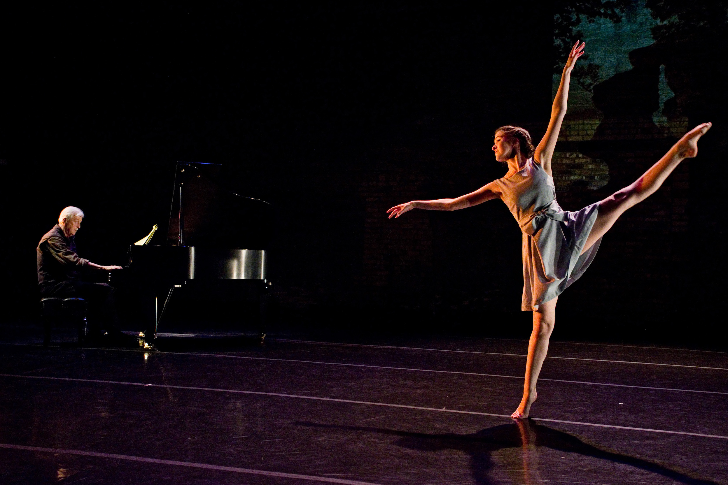 Dancer on releve with leg extended to the side and a pianist playing music