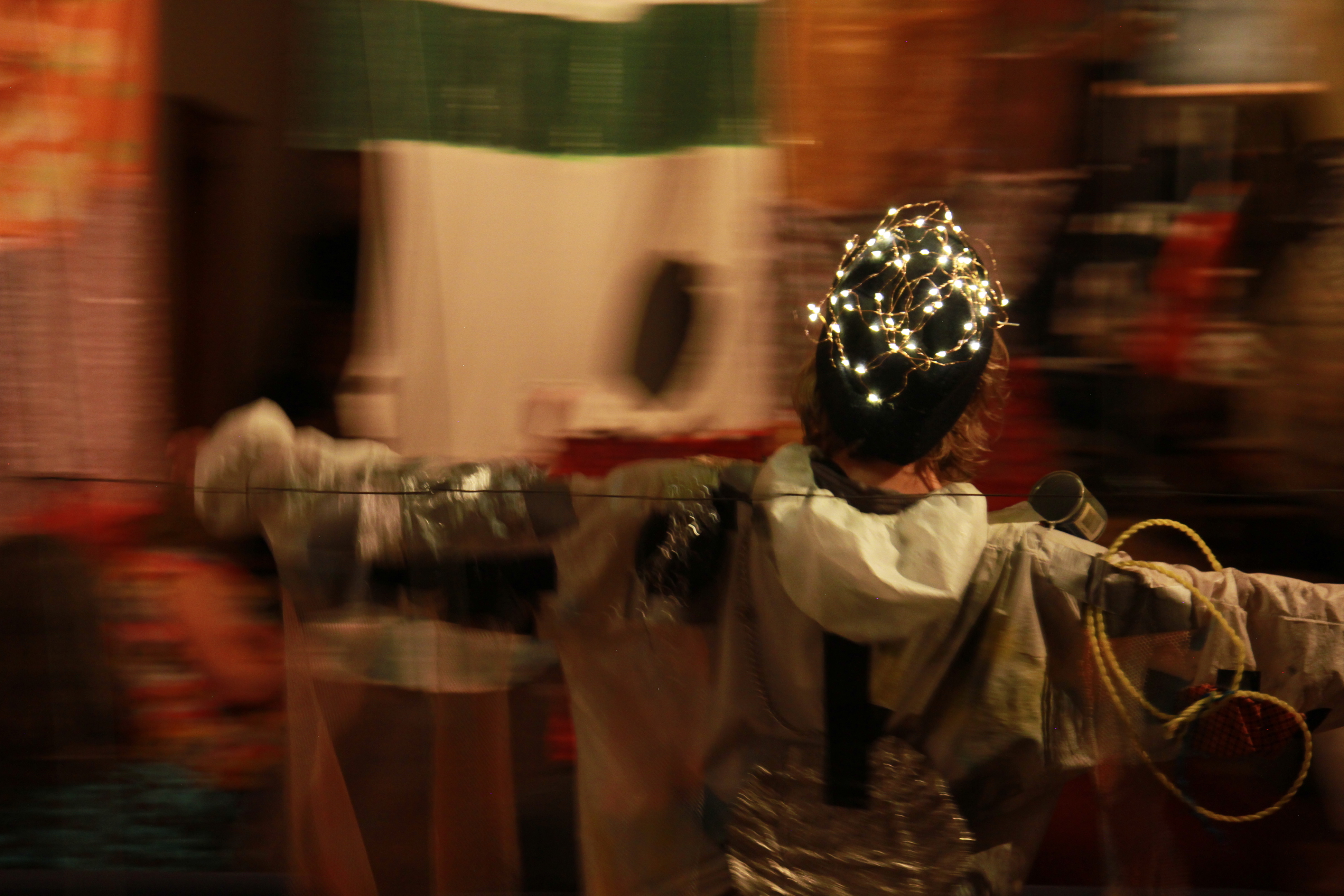 Dancer with arms outstretched wearing a hat of wire and small lights