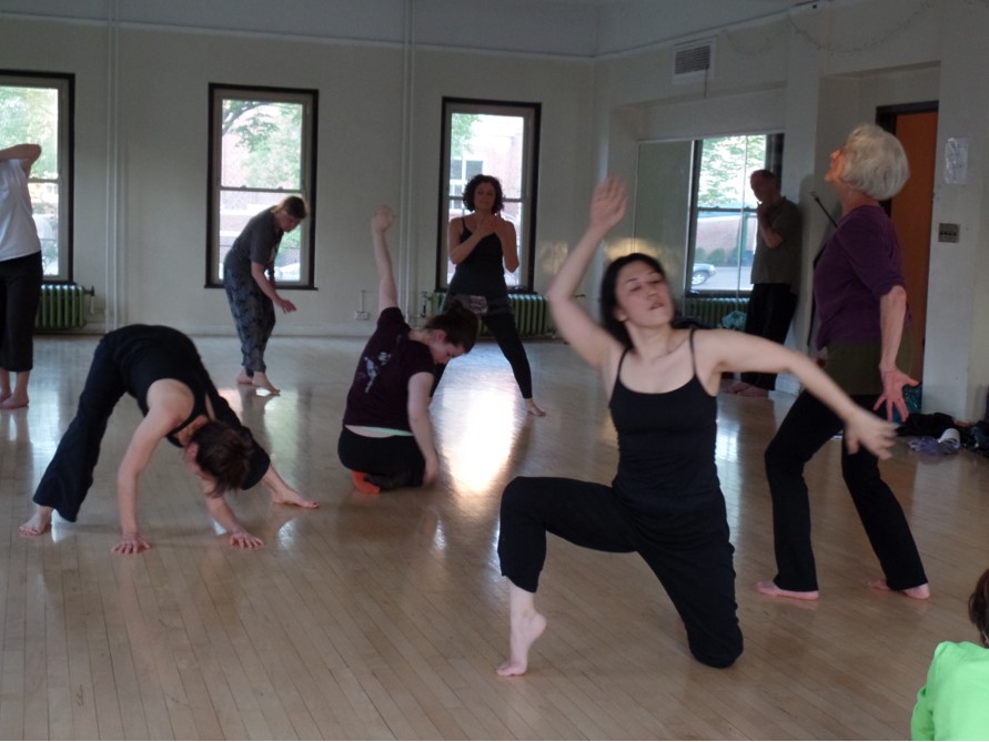 Several dancers in black clothing dance and make shapes in a studio